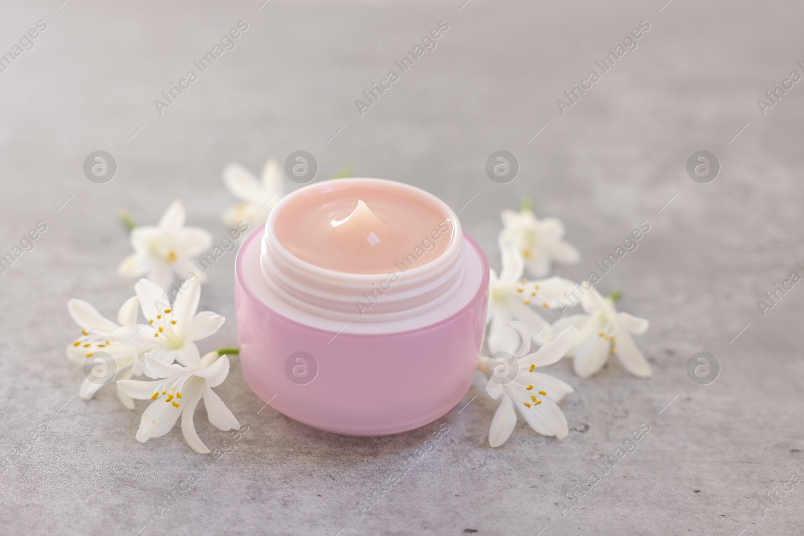 Photo of Cream in jar and beautiful jasmine flowers on grey table, closeup