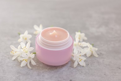 Photo of Cream in jar and beautiful jasmine flowers on grey table, closeup