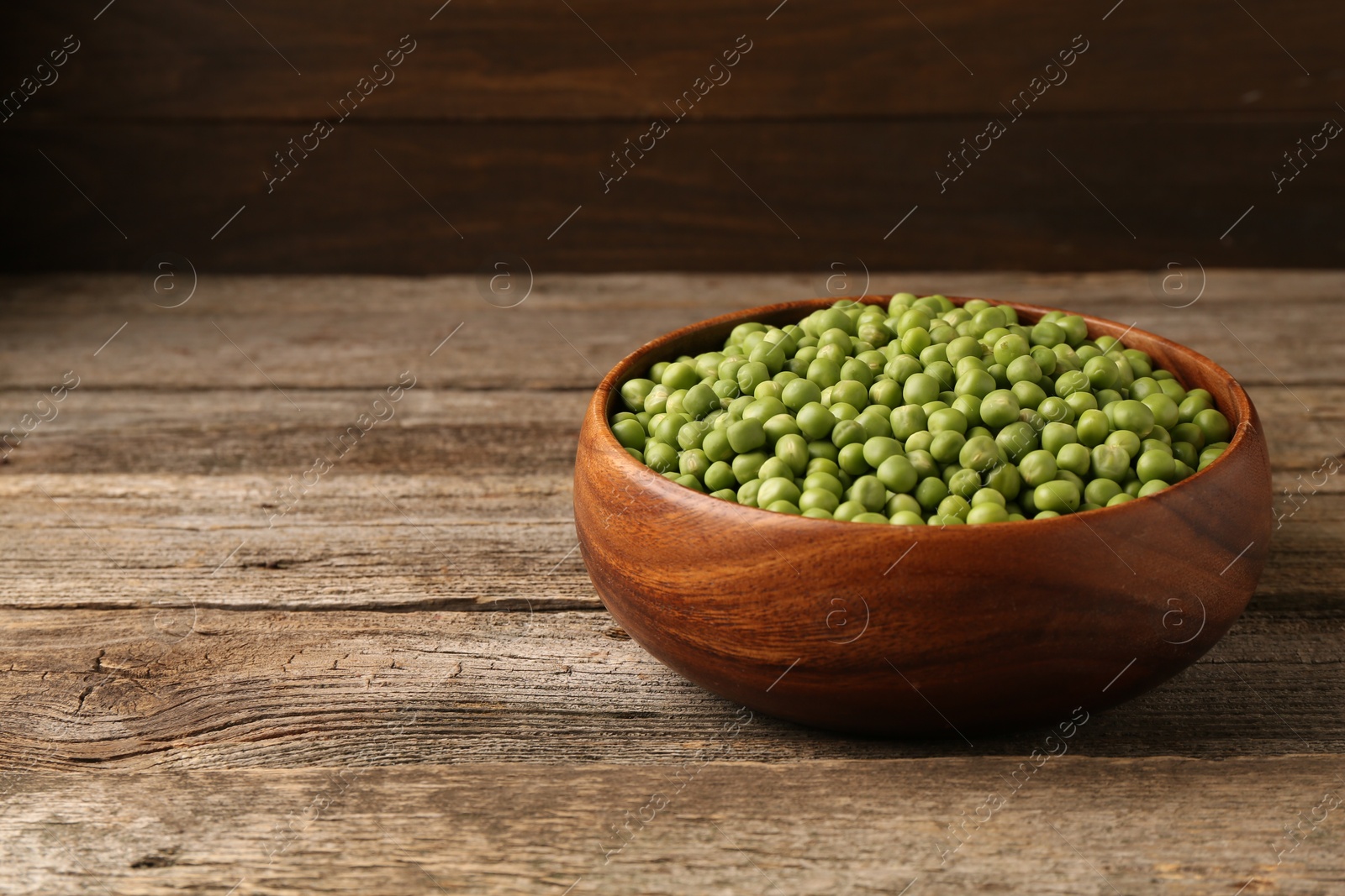 Photo of Fresh green peas in bowl on wooden table, space for text