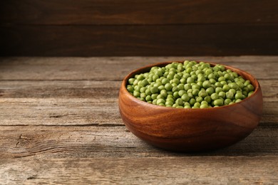 Fresh green peas in bowl on wooden table, space for text