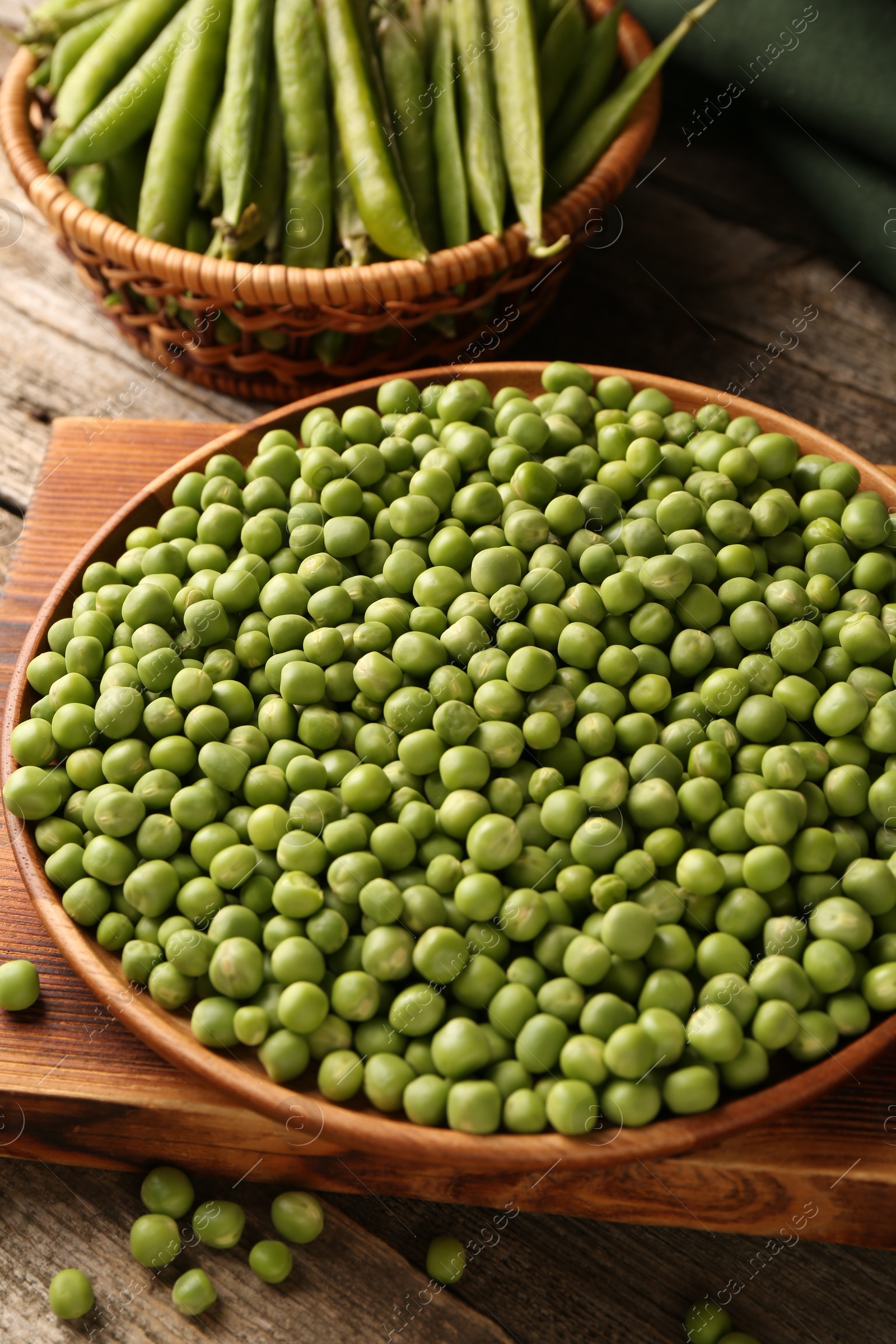 Photo of Fresh green peas in bowl and pods on wooden table, closeup