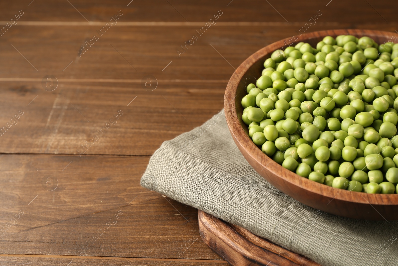 Photo of Fresh green peas in bowl on wooden table, space for text