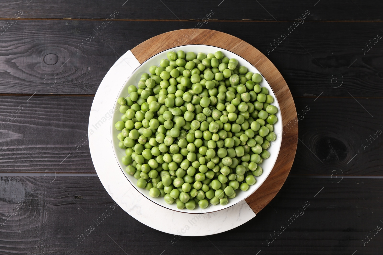 Photo of Fresh green peas in bowl on black wooden table, top view