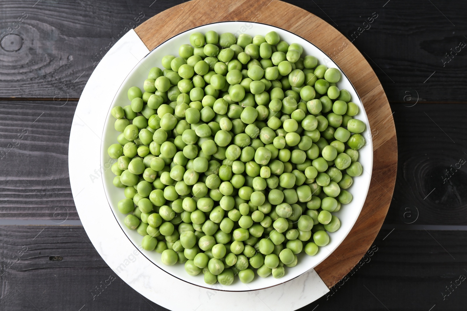 Photo of Fresh green peas in bowl on black wooden table, top view