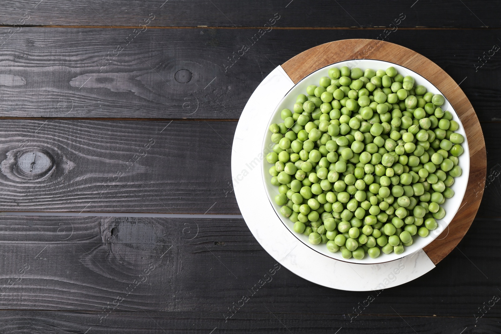 Photo of Fresh green peas in bowl on black wooden table, top view. Space for text