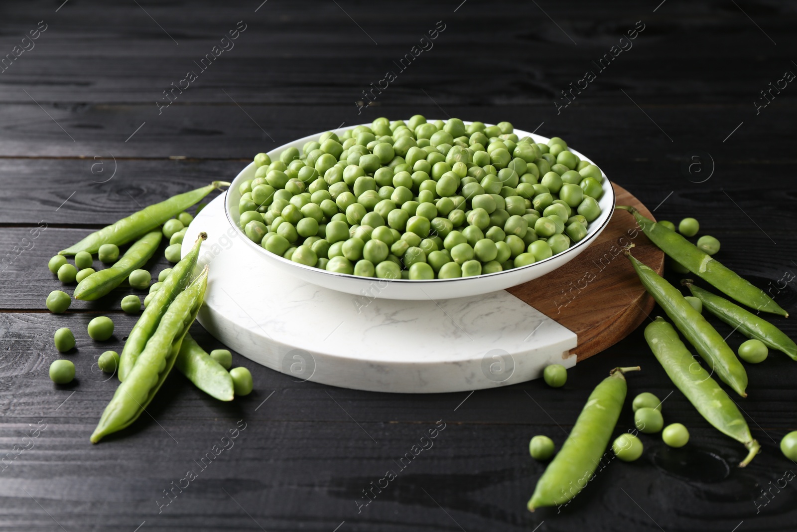 Photo of Fresh green peas in bowl and pods on black wooden table