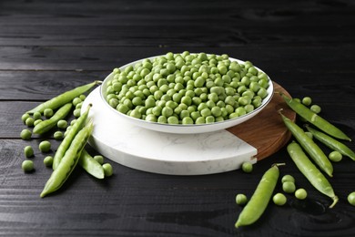 Fresh green peas in bowl and pods on black wooden table