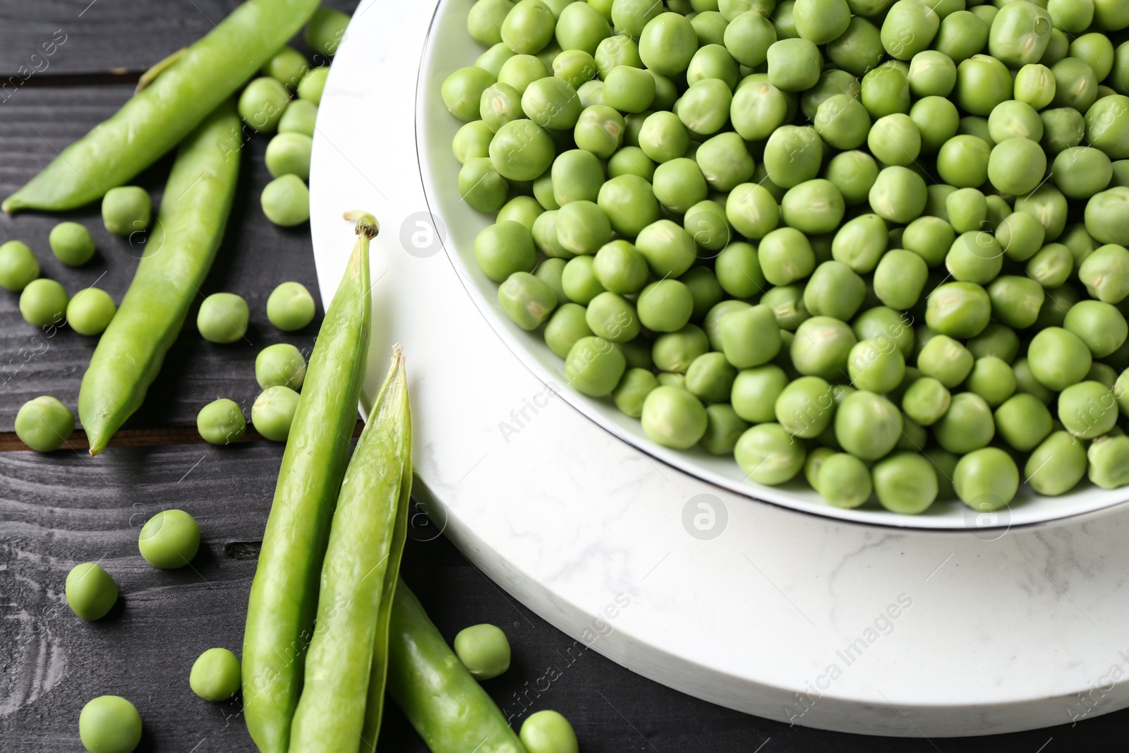 Photo of Fresh green peas in bowl and pods on black wooden table, closeup