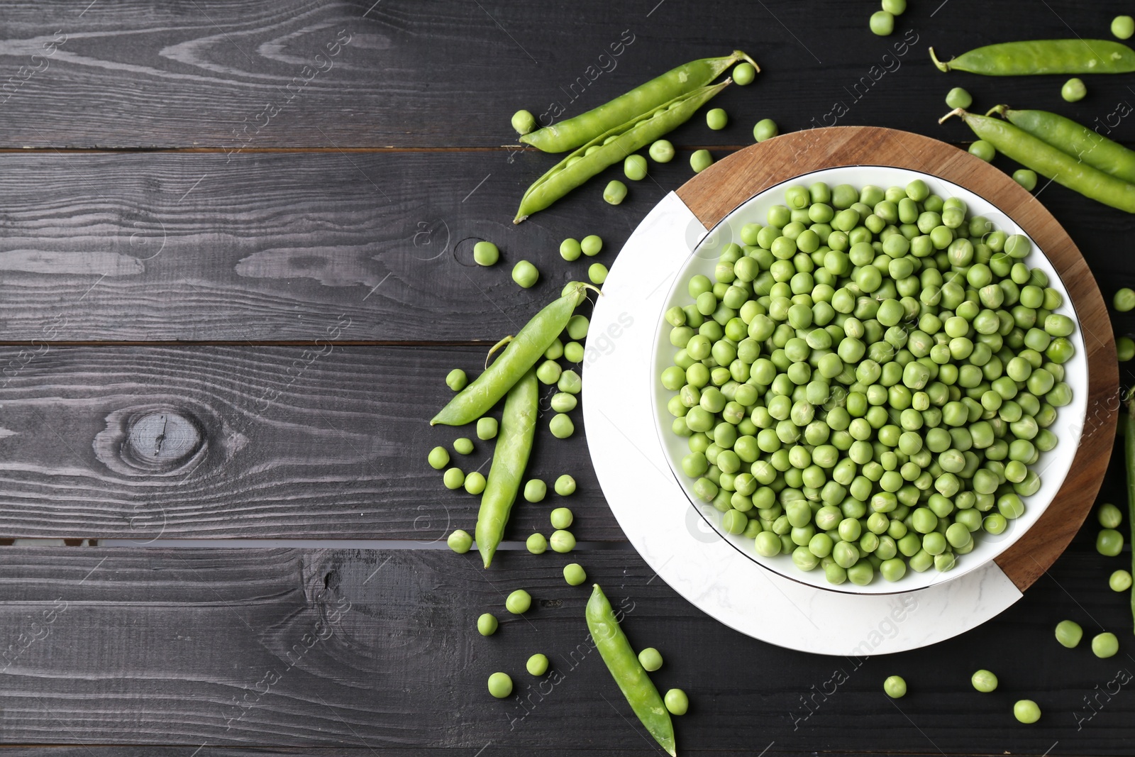 Photo of Fresh green peas in bowl and pods on black wooden table, flat lay. Space for text