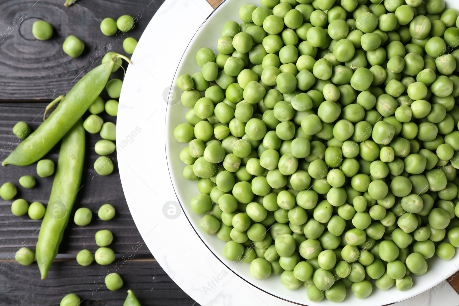 Photo of Fresh green peas in bowl and pods on black wooden table, flat lay