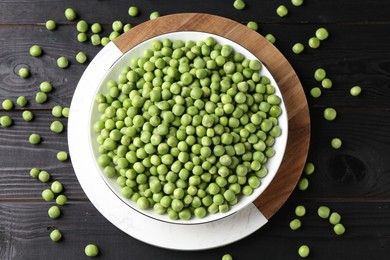 Photo of Fresh green peas in bowl on black wooden table, top view