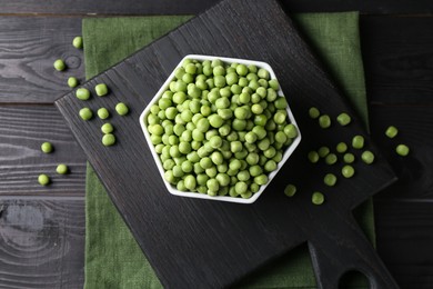 Fresh green peas in bowl on black wooden table, top view