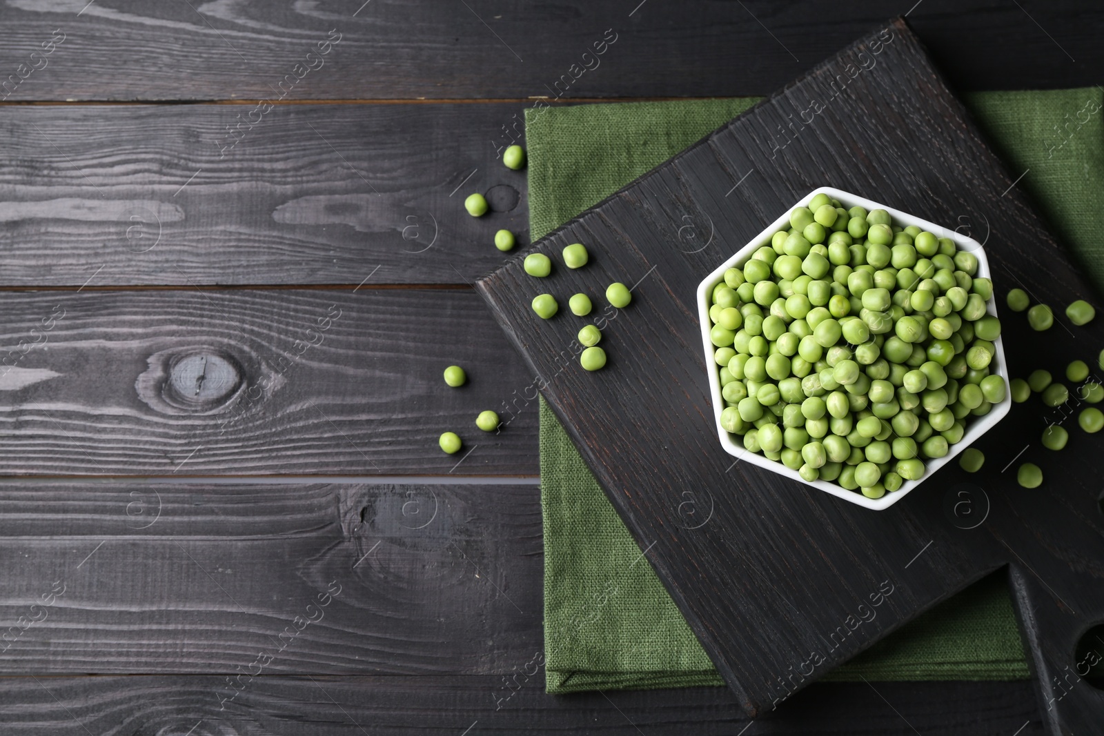 Photo of Fresh green peas in bowl on black wooden table, top view. Space for text