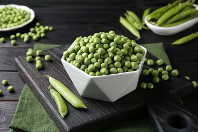 Photo of Fresh green peas in bowl and pods on black wooden table