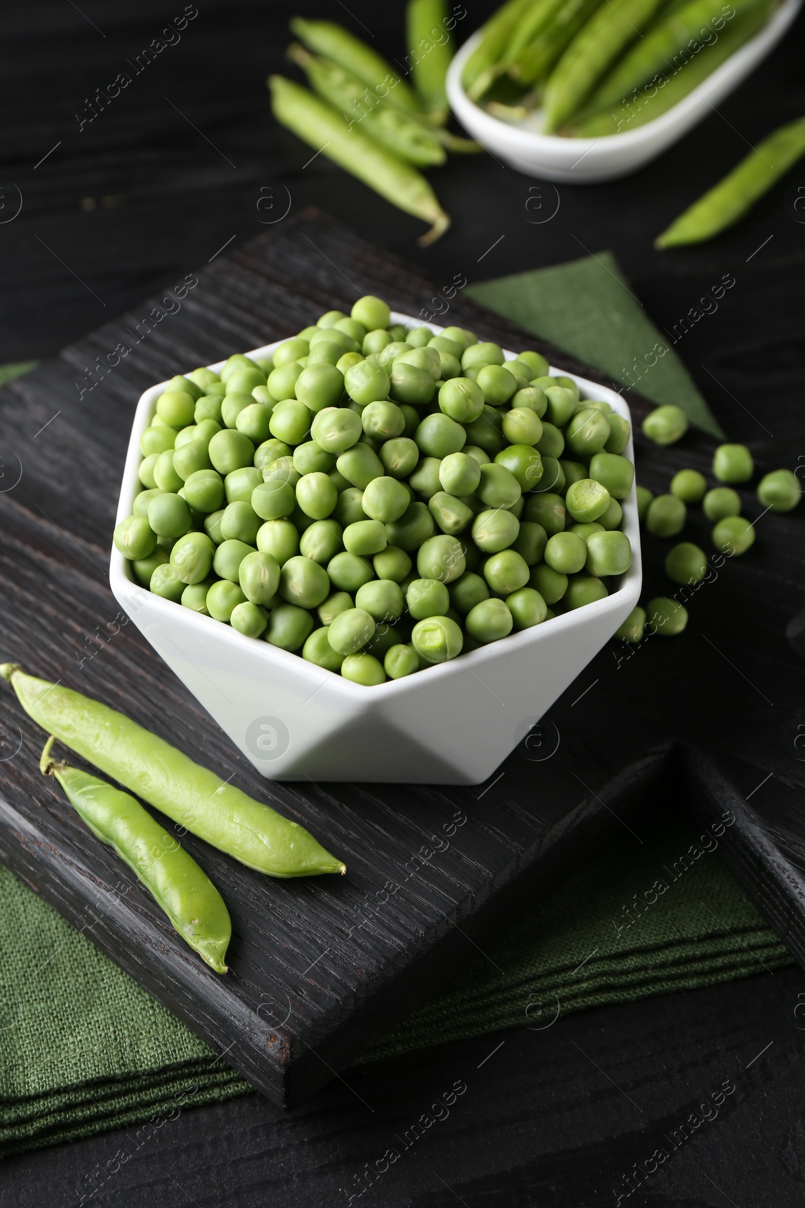 Photo of Fresh green peas in bowl and pods on black wooden table