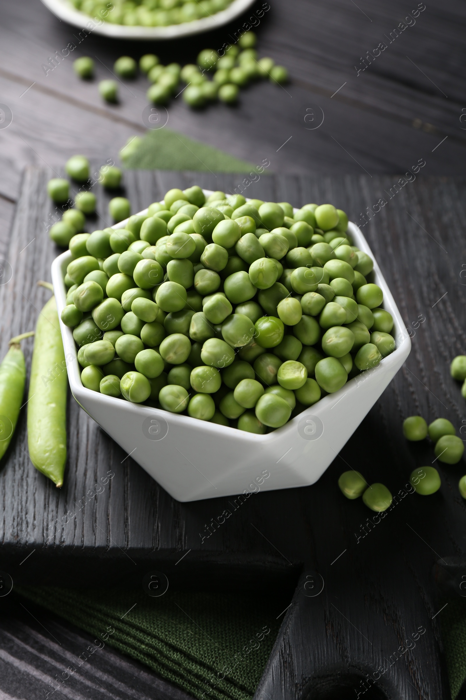 Photo of Fresh green peas in bowl and pods on black wooden table