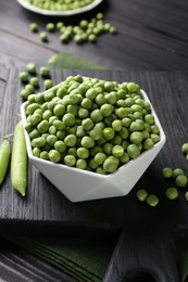 Fresh green peas in bowl and pods on black wooden table