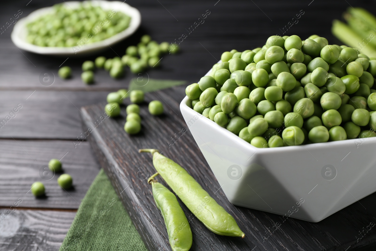 Photo of Fresh green peas in bowl and pods on black wooden table, closeup