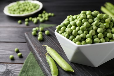 Fresh green peas in bowl and pods on black wooden table, closeup