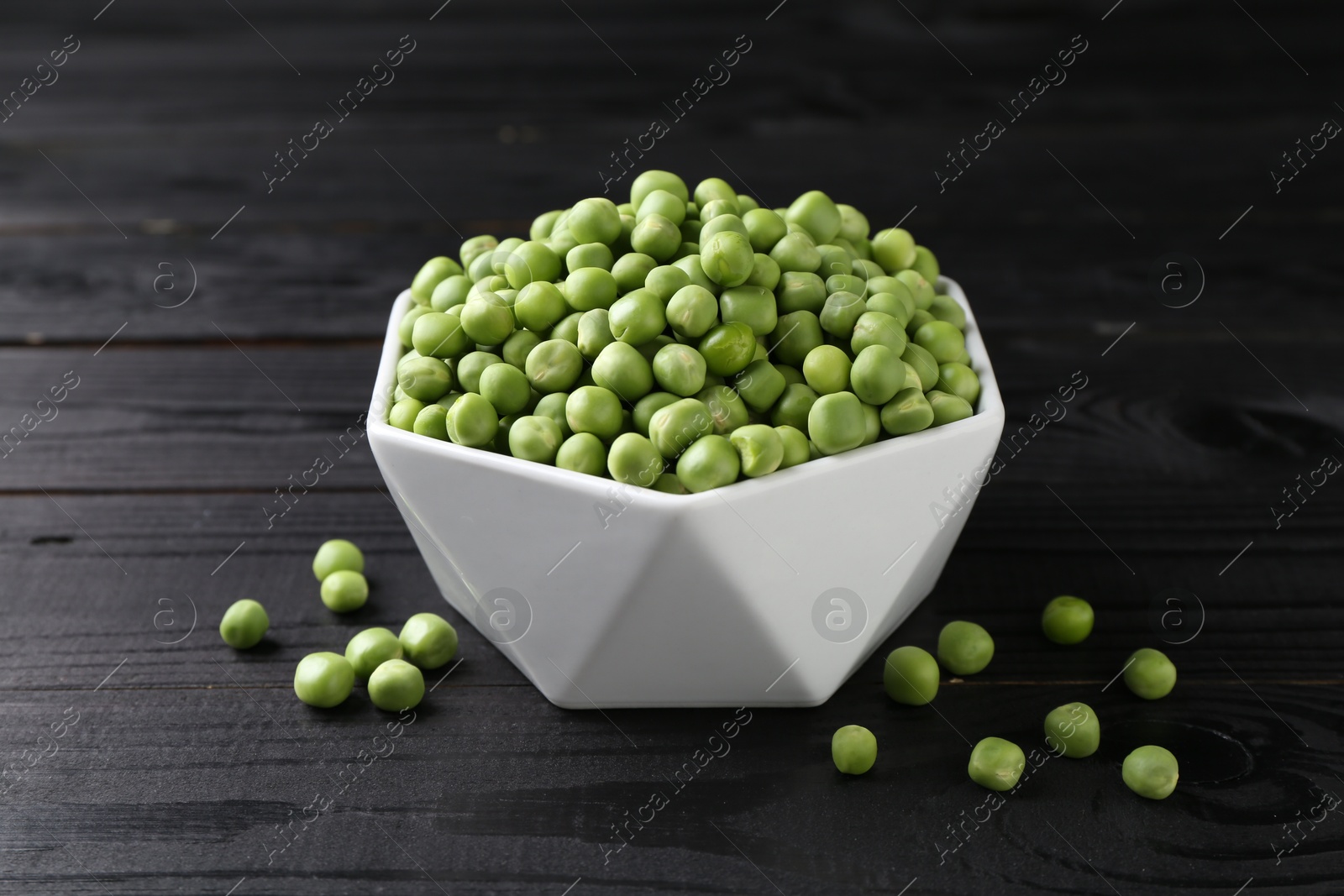 Photo of Fresh green peas in bowl on black wooden table