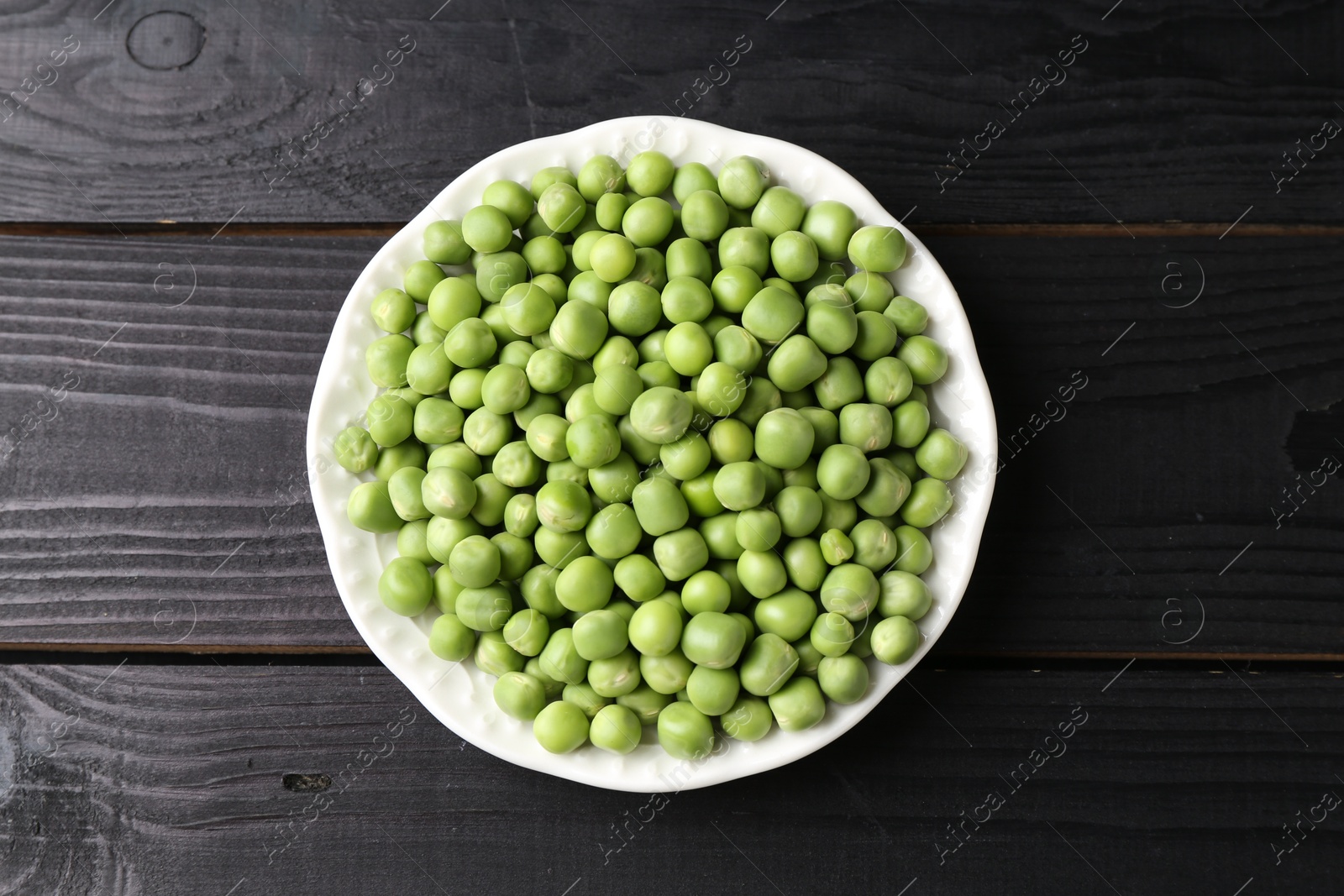 Photo of Fresh green peas in bowl on black wooden table, top view