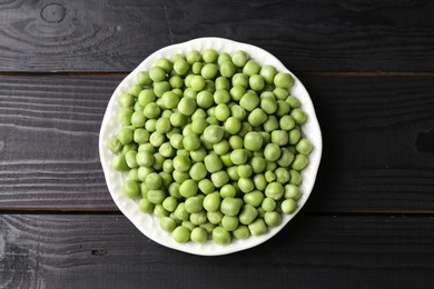 Fresh green peas in bowl on black wooden table, top view