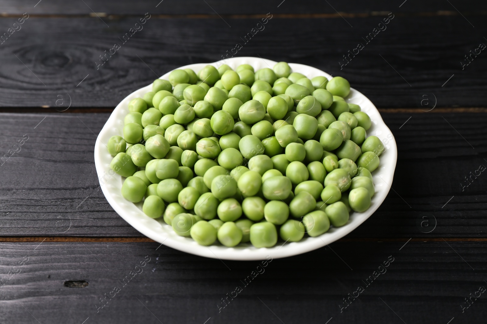 Photo of Fresh green peas in bowl on black wooden table