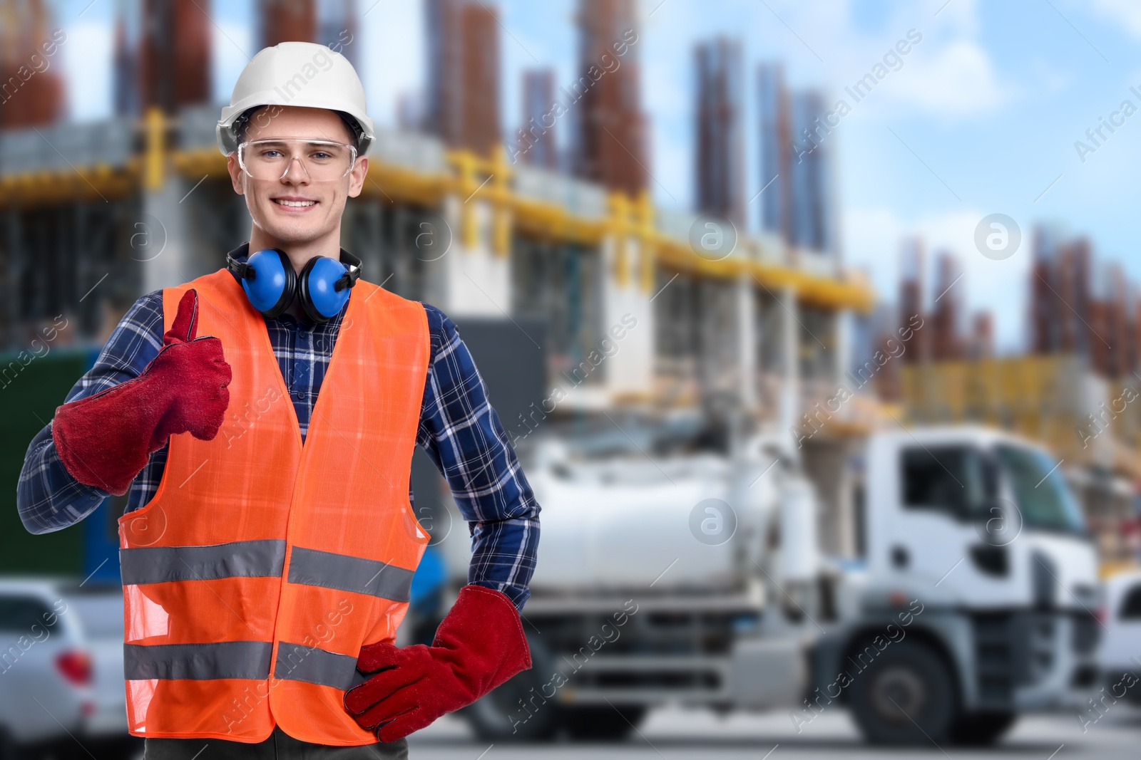 Image of Young man wearing safety equipment and showing thumbs up at construction site. Space for text