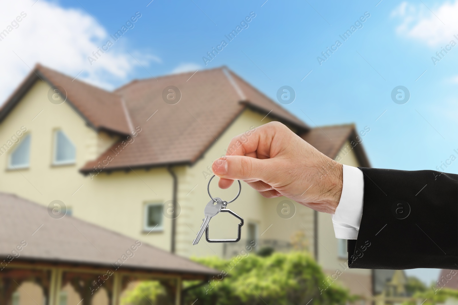 Image of Real estate agent holding house key against beautiful dwelling, closeup