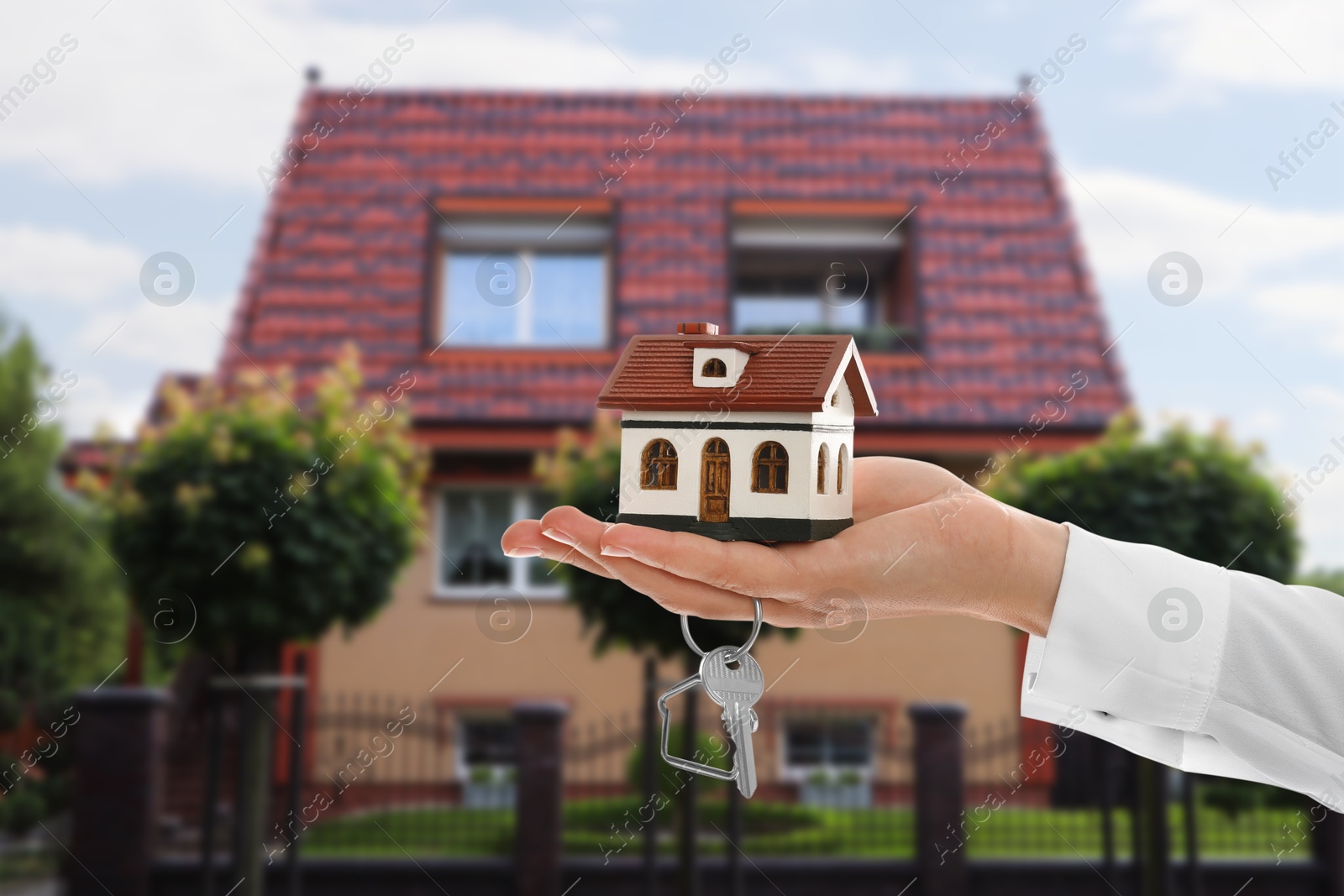 Image of Real estate agent holding house model and key against future dwelling, closeup