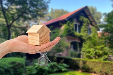 Real estate agent holding house model and key against future dwelling, closeup