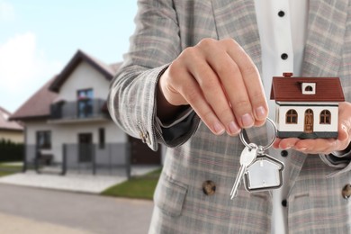 Real estate agent holding house model and key against future dwelling, closeup