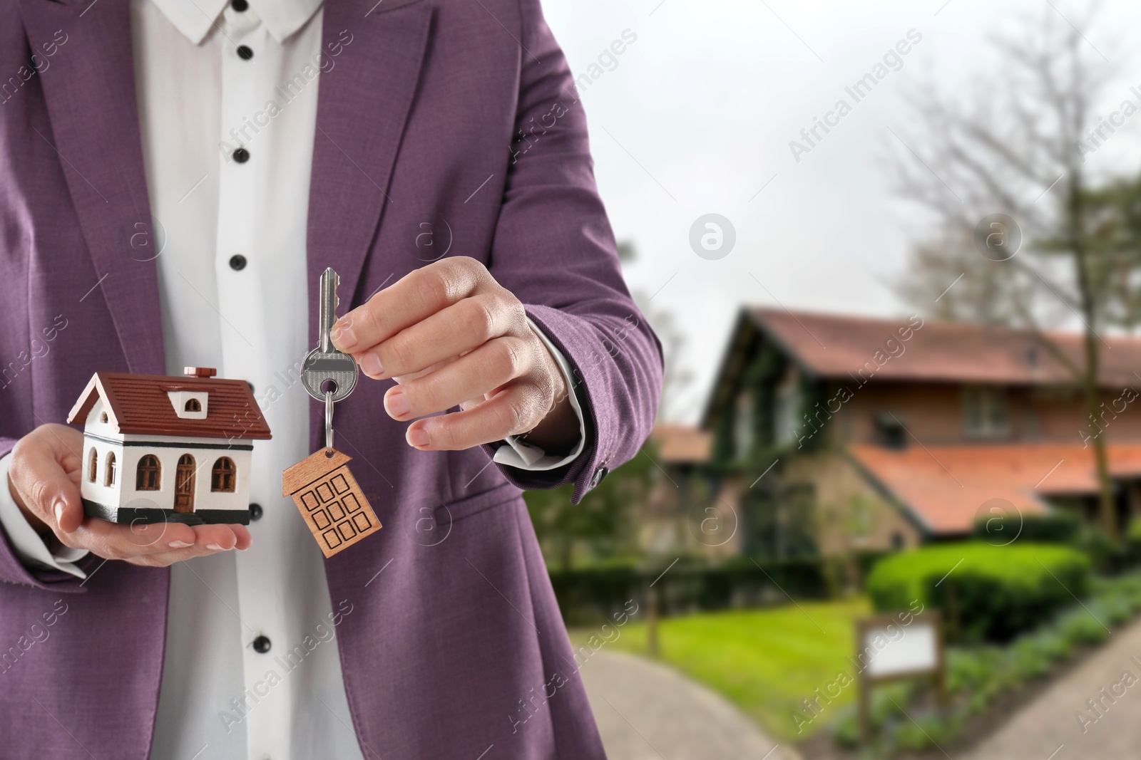 Image of Real estate agent holding house model and key against future dwelling, closeup