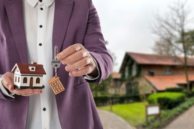 Image of Real estate agent holding house model and key against future dwelling, closeup