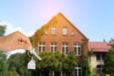 Image of Real estate agent holding house key against beautiful dwelling, closeup