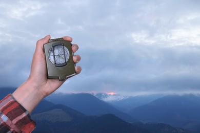 Woman using compass in mountains, closeup. Navigational instrument