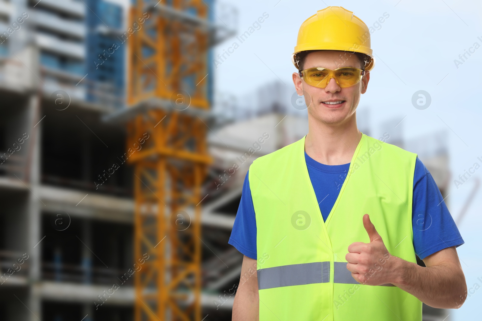 Image of Young man wearing safety equipment and showing thumbs up at construction site. Space for text