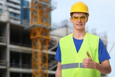 Image of Young man wearing safety equipment and showing thumbs up at construction site. Space for text