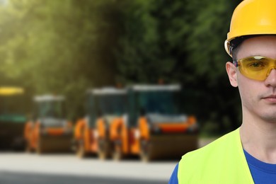 Image of Young man wearing safety equipment and road repair service rollers on background. Space for text