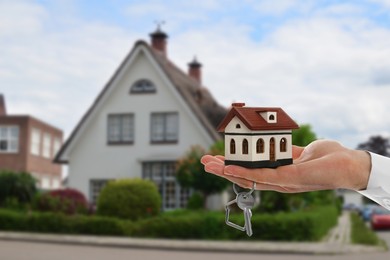 Image of Real estate agent holding house model and key against future dwelling, closeup