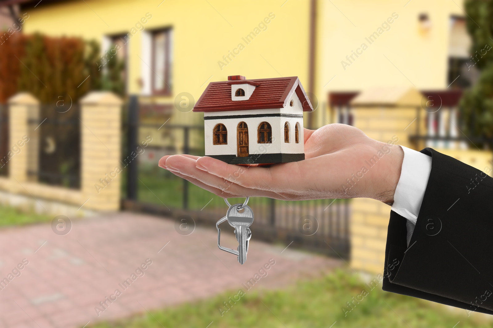 Image of Real estate agent holding house model and key against future dwelling, closeup