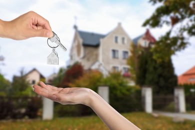 Real estate agent giving house key to new owner against beautiful dwelling, closeup