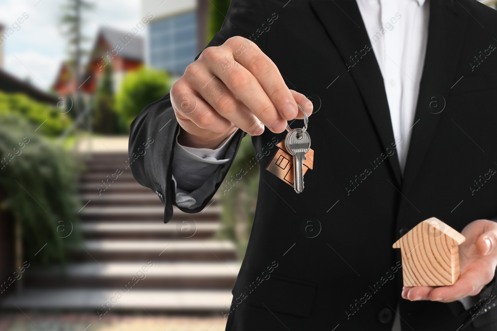 Image of Real estate agent holding house model and keys against future dwelling, closeup