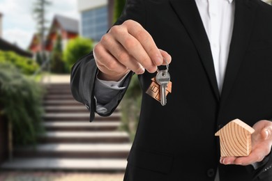 Image of Real estate agent holding house model and keys against future dwelling, closeup