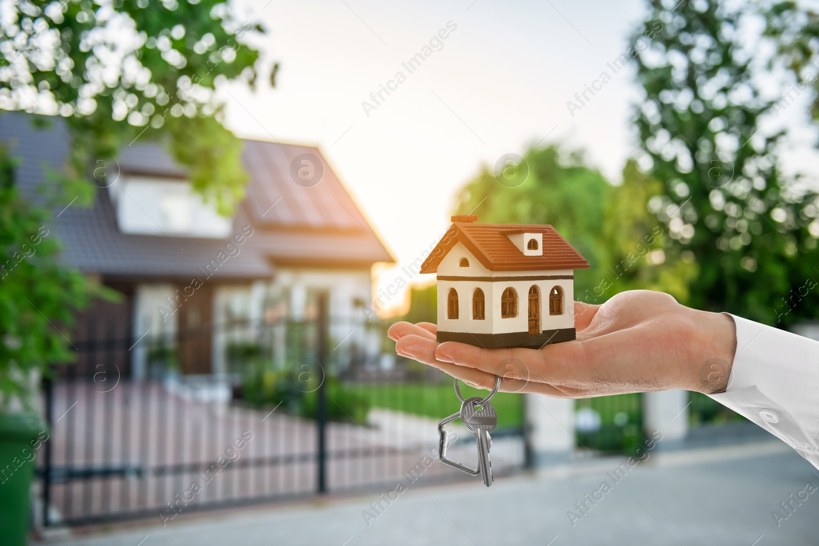 Image of Real estate agent holding house model and key against future dwelling, closeup