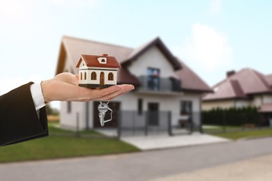 Real estate agent holding house model and key against future dwelling, closeup