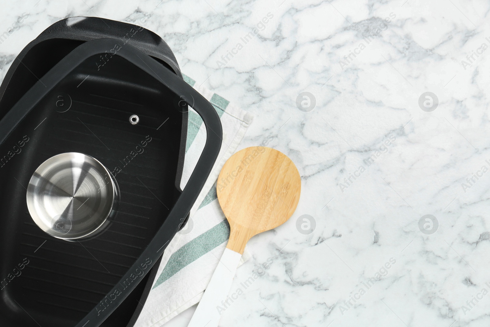 Photo of Black pot with glass lid and round spatula on white marble table, flat lay. Space for text