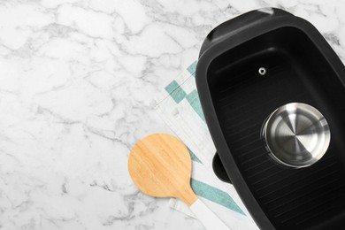 Photo of Black pot with glass lid and round spatula on white marble table, flat lay. Space for text