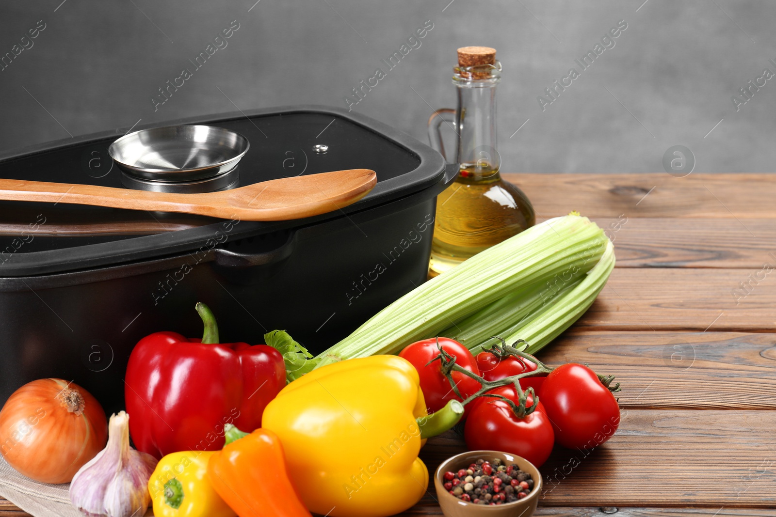 Photo of Black pot with glass lid, different products and spoon on wooden table