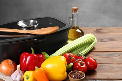 Photo of Black pot with glass lid, different products and spoon on wooden table